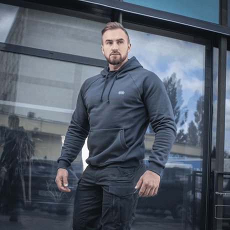 Mand iklædt M-Tac Hættetrøje Cotton Raglan foran glasbygning, bærer afslappet og komfortabelt look, perfekt til hverdagsbrug.