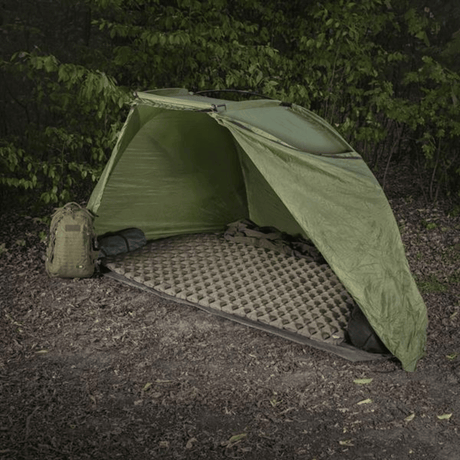 M-Tac Oppusteligt Liggeunderlag 195x120 sat op i et grønt telt i skovområder, ideelt til camping og beskyttelse mod ujævnt terræn og kulde