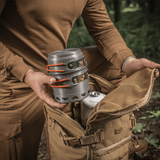 Person pakker M-Tac Individuelt Kogesæt til Brænder i rygsæk i skoven, ideelt til friluftsliv og camping, fremstillet af anodiseret aluminium.