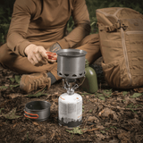 M-Tac Individuelt Kogesæt til Brænder til camping i skoven, med en mand der bruger sættet på brænderen under udendørs ophold.