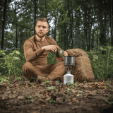 Mand i skov bruger M-Tac Individuelt Kogesæt til Brænder til camping, sidder ved komfur med rygsæk.