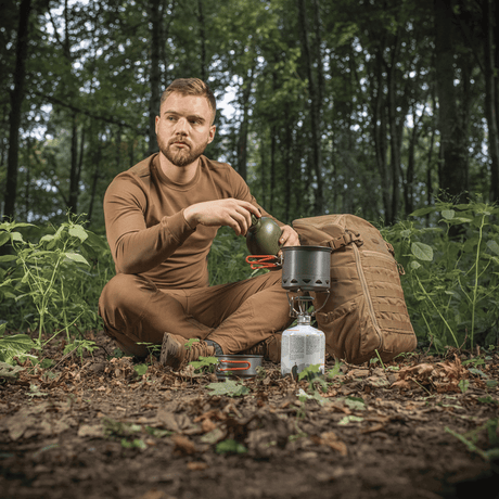 Mand i skov bruger M-Tac Individuelt Kogesæt til Brænder til camping, sidder ved komfur med rygsæk.