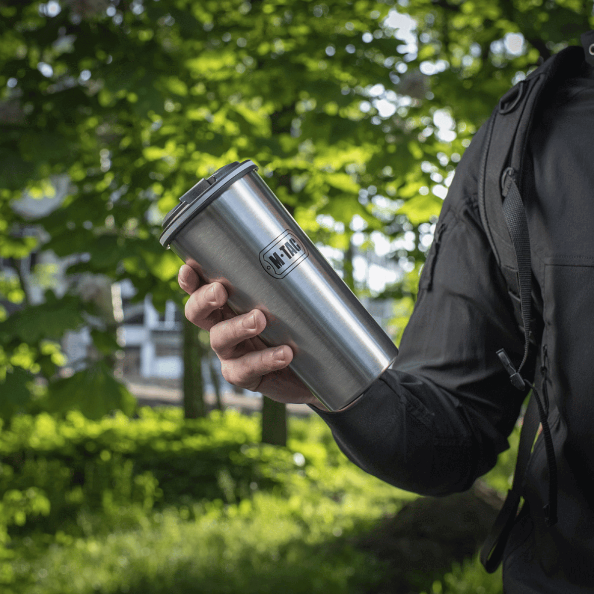 Person holder en M-Tac Termokop 450 ml med Ventil i en grøn skov.