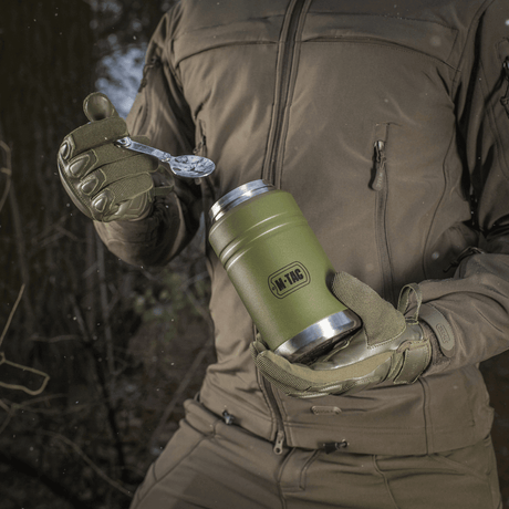 M-Tac Termoflaske 750 ml med Folde-ske bruges udendørs, vist med moderne design og praktisk foldeske, perfekt til camping og vandreture.