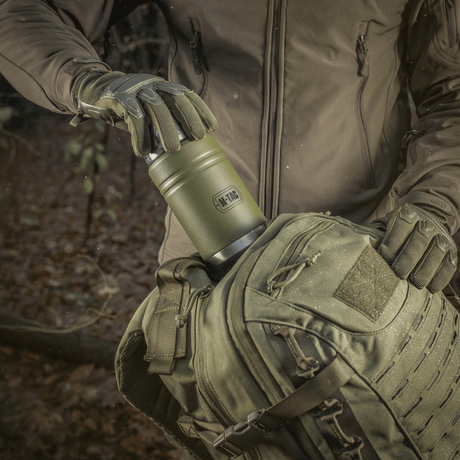 M-Tac Termoflaske 750 ml med Folde-ske til camping i skovmijø, robust design, god til varme drikke, ideel til udendørs brug og eventyr.