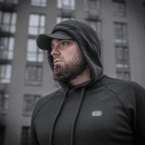 Mand iført M-Tac Cotton Raglan Hard Hoodie, 100% bomuld, med fleecefor, stilfuld til hverdagsbrug, set foran bybygning.