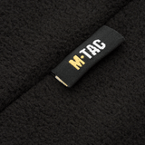 Nærbillede af M-Tac Delta Fleece Jakke etikette, sort og gul logo, fleece materiale, ideel til udendørs og kolde vejrforhold