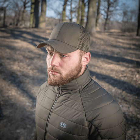 Mand iført M-Tac Mesh Flex Ripstop Baseball Cap i en skov, viser kasketens mesh-paneler og holdbar design til udendørs brug.