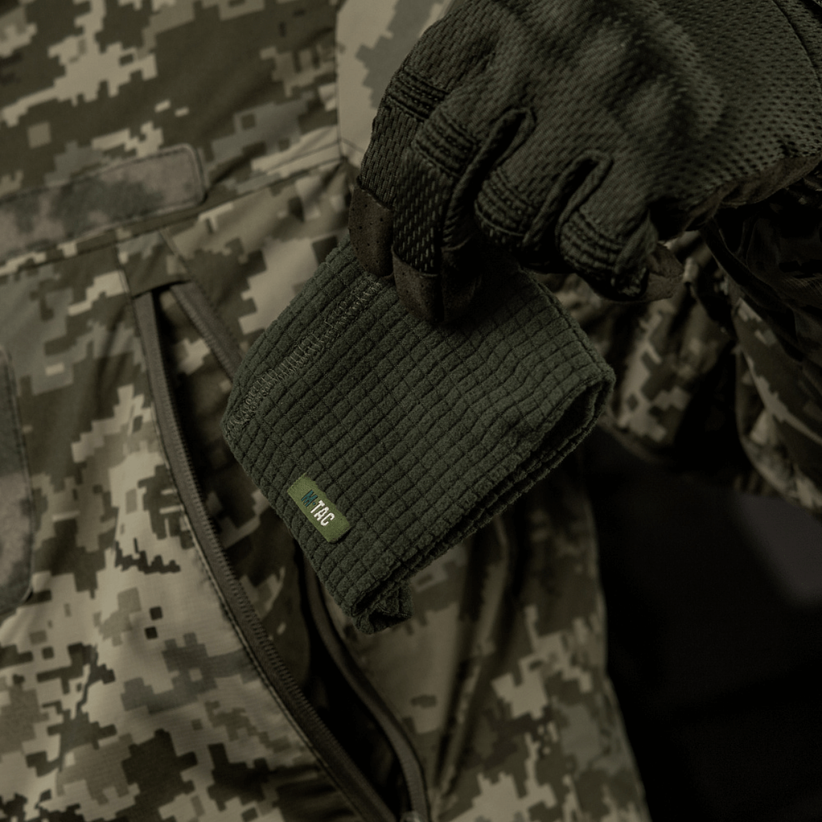 M-Tac Rip-Stop Fleece Hjelmliner - varm og slidstærk fleece hjelmliner i hånden, perfekt til køligt vejr, set mod camouflagebaggrund.