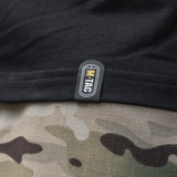 Nærbillede af M-Tac T-Shirt Surf Club tag, sort stof med kamuflagerprint i baggrunden