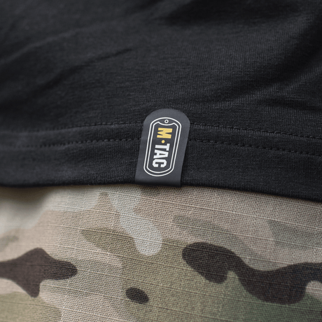 Nærbillede af M-Tac T-Shirt Surf Club tag, sort stof med kamuflagerprint i baggrunden