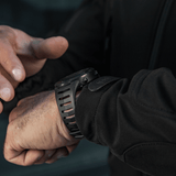 Person justerer M-Tac Tactical Ur 2147 på håndled. Ideel til outdoor og taktisk brug med robust design og praktiske funktioner.