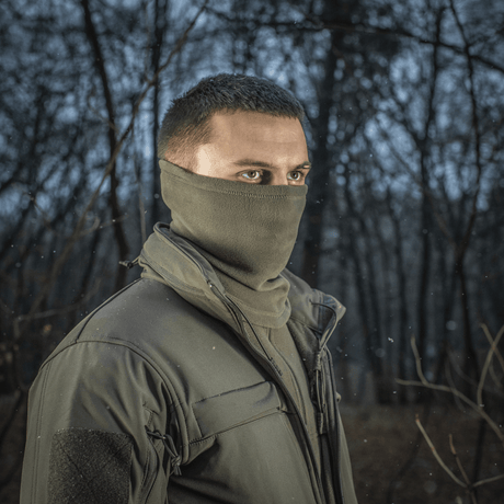 Mand bærer M-Tac Tube Scarf Polartec i skov omgivelser, stilfuldt og varmt halstørklæde til udendørs aktiviteter i kolde årstider.
