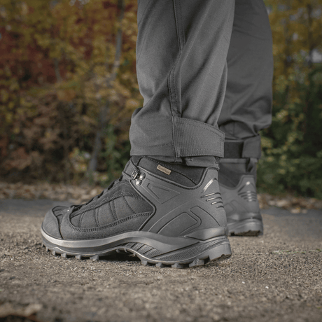 Person iført M-Tac Taktiske Bukser Patriot Gen. II Flex stående på grusvej med sorte taktiske støvler, efterårsbaggrund.