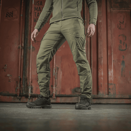 M-Tac Taktiske Bukser Aggressor Gen. II Flex i grøn farve mod en industriel baggrund