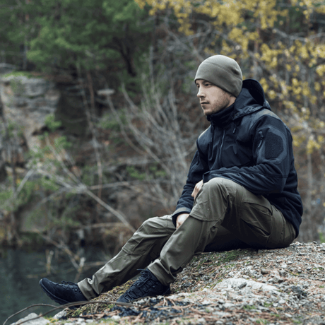 Mand iført M-tac Taktiske Bukser Conquistador Gen. I Flex sidder udendørs med natur i baggrunden.