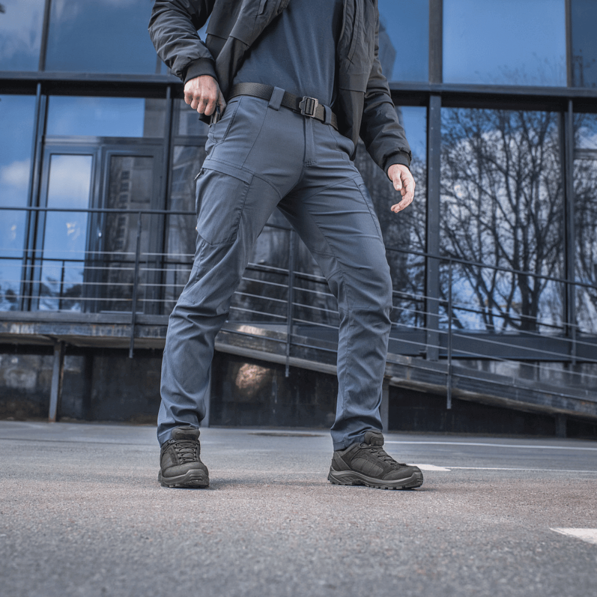 Mand iført M-Tac Bukser Sahara Flex Light foran en moderne bygning, fremhæver buksernes fleksibilitet og stilfuldt design.
