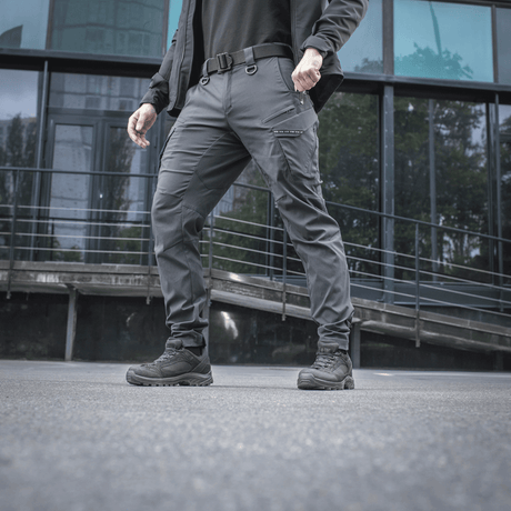 Mand iført M-Tac Bukser Aggressor Summer Flex foran moderne bygning, viser letvægt Rip-Stop nylonstof ideelt til varmt vejr.