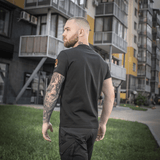 Mand bærer en M-Tac T-shirt Black Sea Expedition foran moderne bygninger