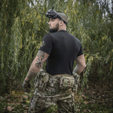 Mand i taktisk udstyr iført M-Tac T-Shirt Delivery Service med FPV-briller står i naturen, klar til aktion.